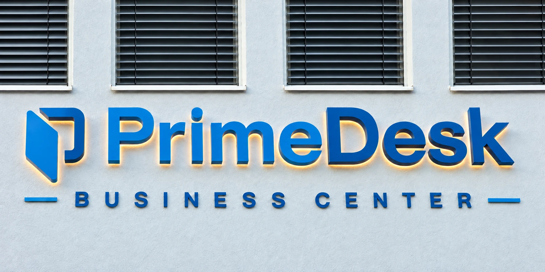 Die blauen PrimeDesk-Einzelbuchstaben an der hellen Fassade mit dezenter Hintergrundbeleuchtung